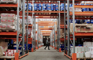 An operator walking in a warehouse surrounded by multiple shelves containing a variety of building supplies.